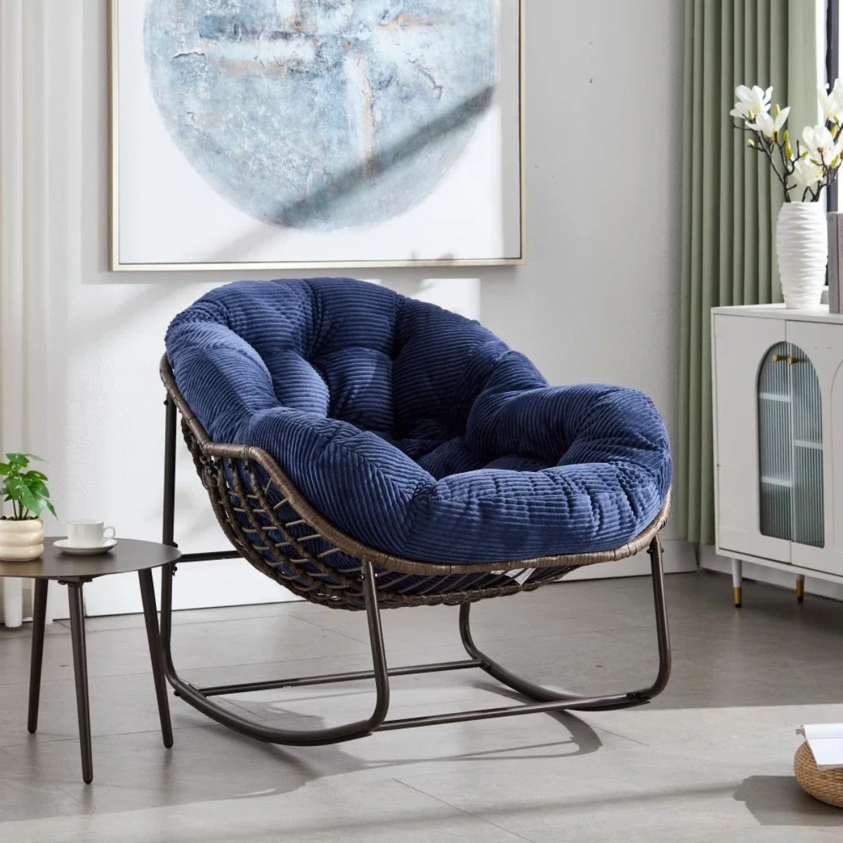 Blue cushioned chair in a modern living room setting with a painting and cabinet in the background.