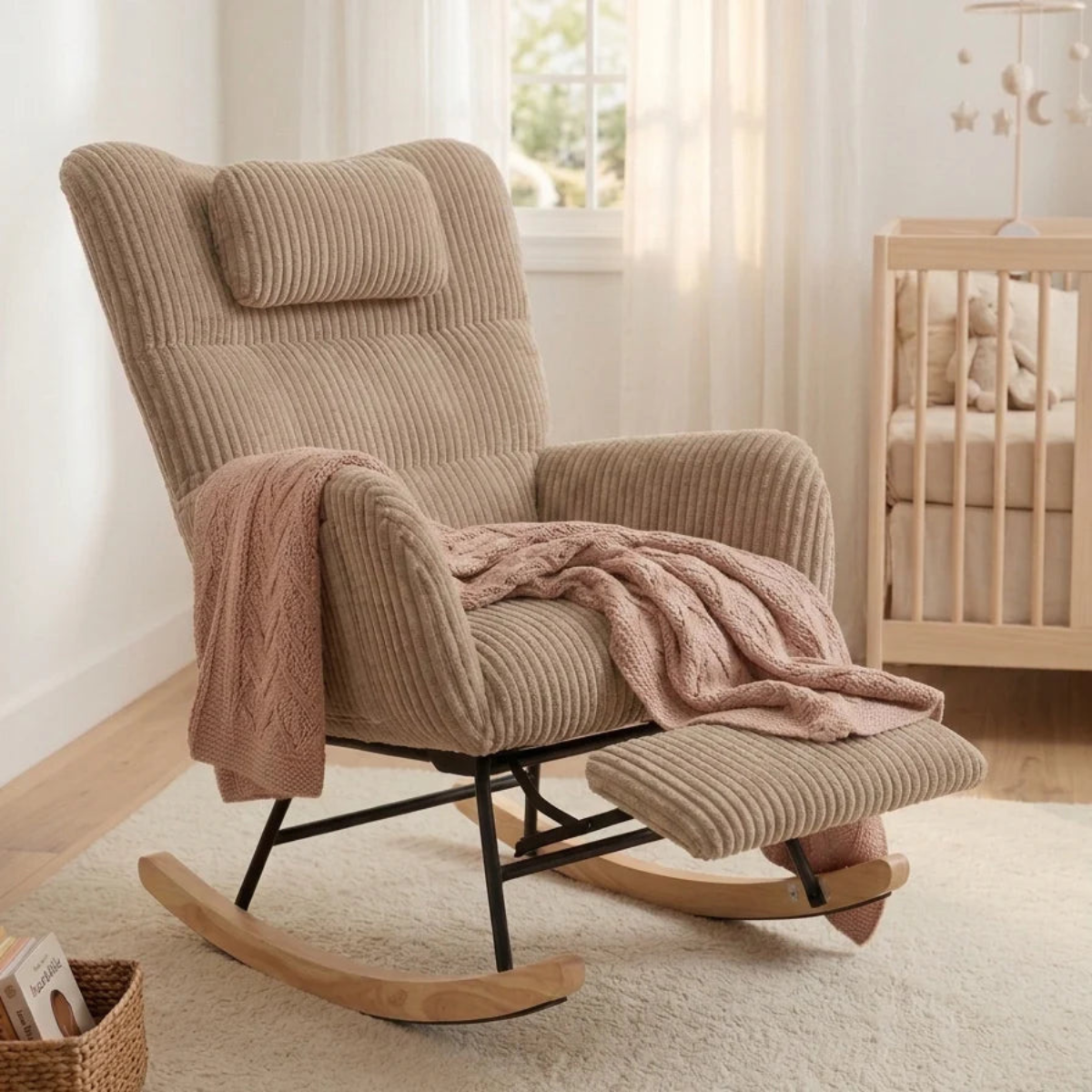 A beige corduroy recliner chair with a matching footrest and pink knit throw blanket, styled in a bright nursery next to a wooden crib.