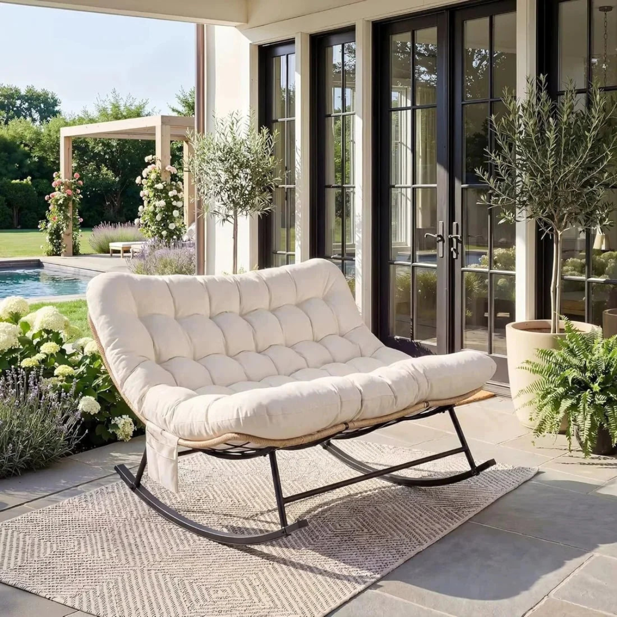 Beige outdoor rocking chair on a patio with plants and a pool in the background