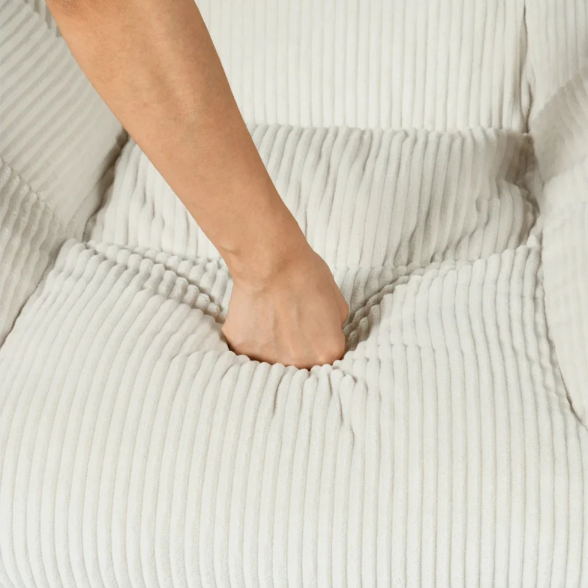 A close-up of a person's hand pressing into the center of a ribbed, off-white corduroy fabric surface, showing the texture and elasticity of the material.