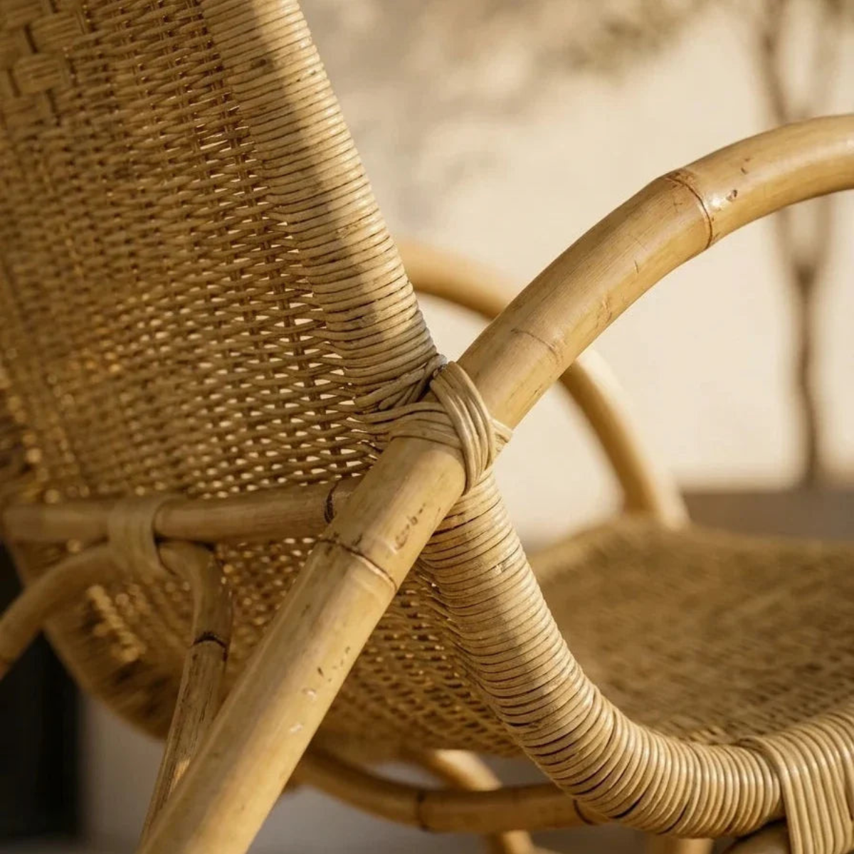 Close-up of a rattan and bamboo chair showing the woven backrest, seat, and curved bamboo armrests in warm natural light.