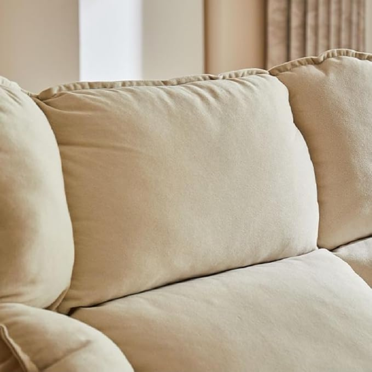 Close-up of a beige upholstered sofa cushion with soft, plush fabric and a subtle tufted edge detail.