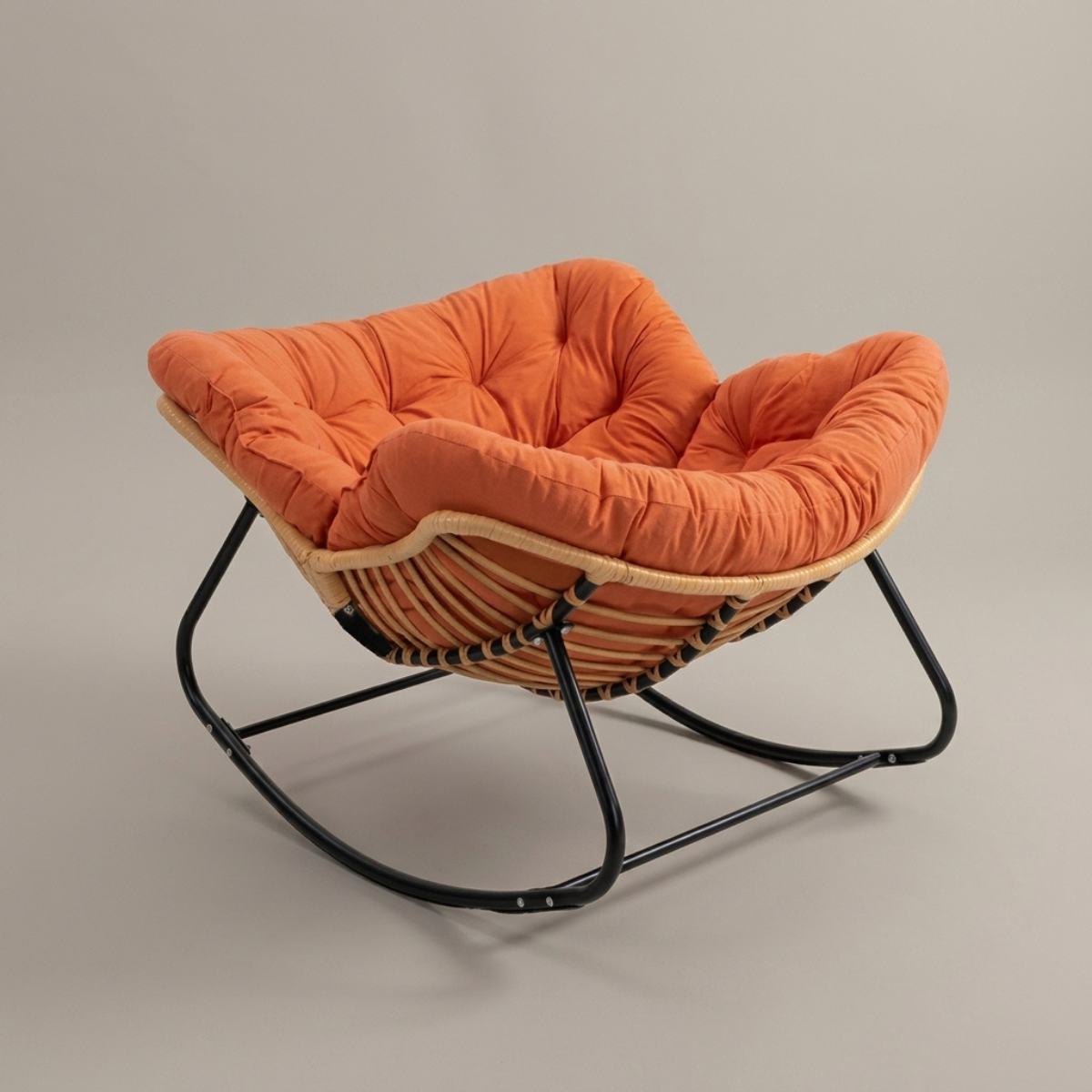 An orange tufted cushioned accent chair with a woven rattan seat and a black metal rocking base, shown against a neutral gray studio background.