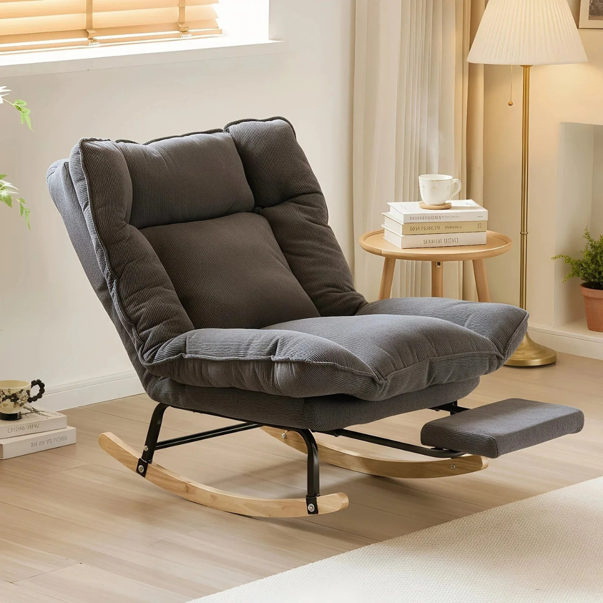 Gray rocking chair in a cozy living room setting with books and a cup on a small table.