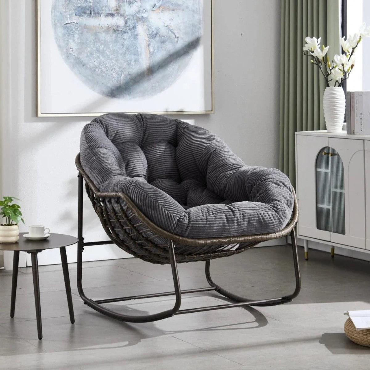 Gray cushioned chair in a modern living room setting with a painting and cabinet in the background.
