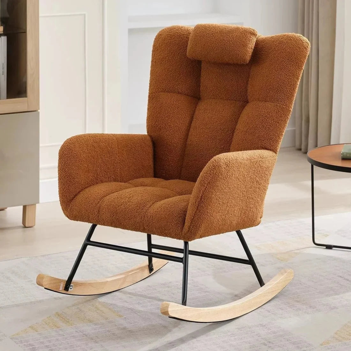 Brown rocking chair in a room with a rug and table.