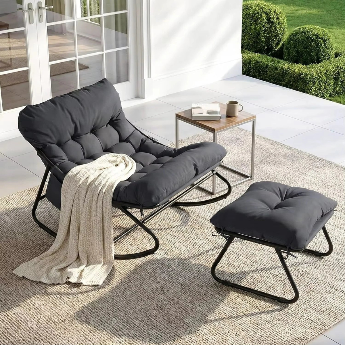 Gray lounge chair with ottoman on a patio with a white wall and greenery in the background