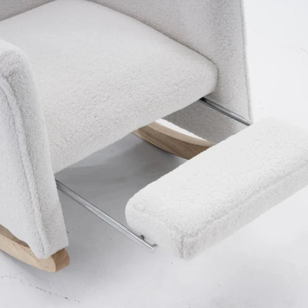 Close-up of a white textured upholstered chair with a footrest extended, showing light wood legs and chrome metal support bars on a white floor.