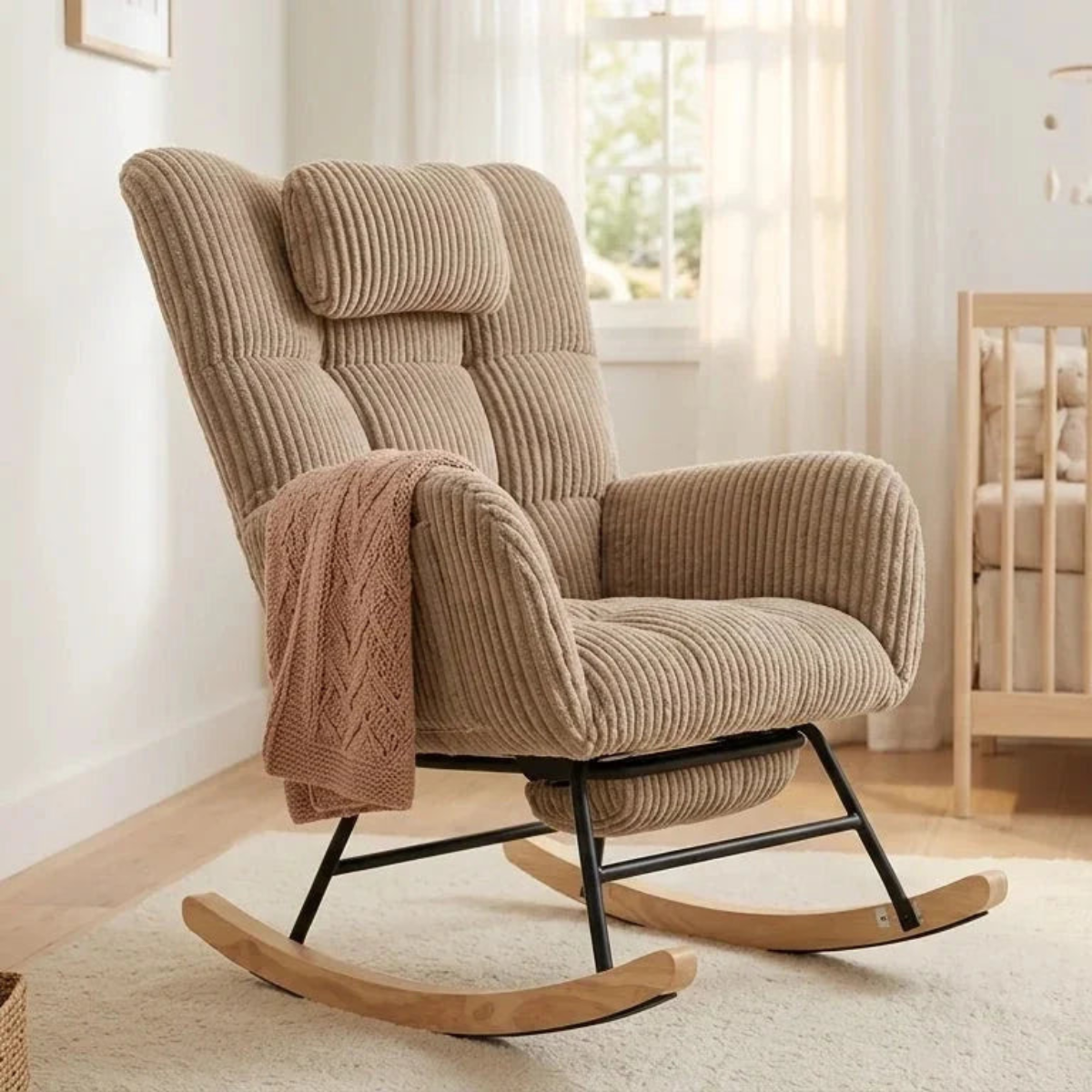 A beige corduroy rocking chair with a matching headrest pillow and a draped pink knit throw blanket, set in a bright, modern nursery room.