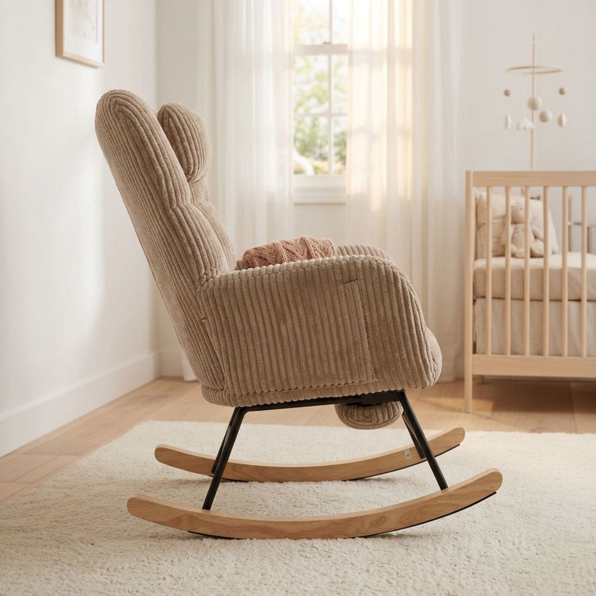 A beige corduroy rocking chair with a high back and black metal legs, styled in a bright, modern nursery next to a wooden crib.