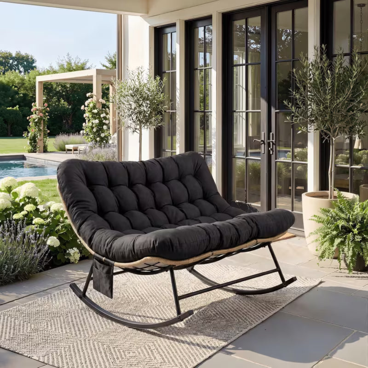 Black cushioned rocking chair on a patio with a garden view