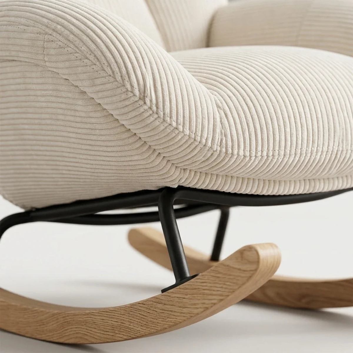 Close-up of a modern upholstered rocking chair with cream ribbed corduroy fabric, a black metal frame, and light natural wood rockers on a white background.