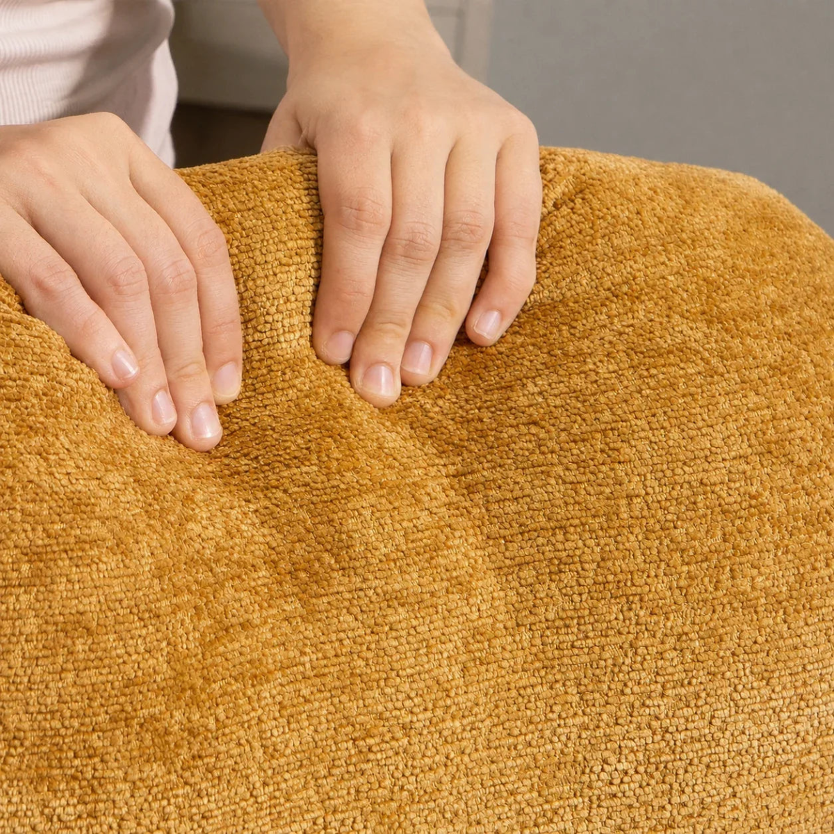 Close-up of a person's hands pressing down on a textured mustard yellow bath mat to show its plush, looped fabric.
