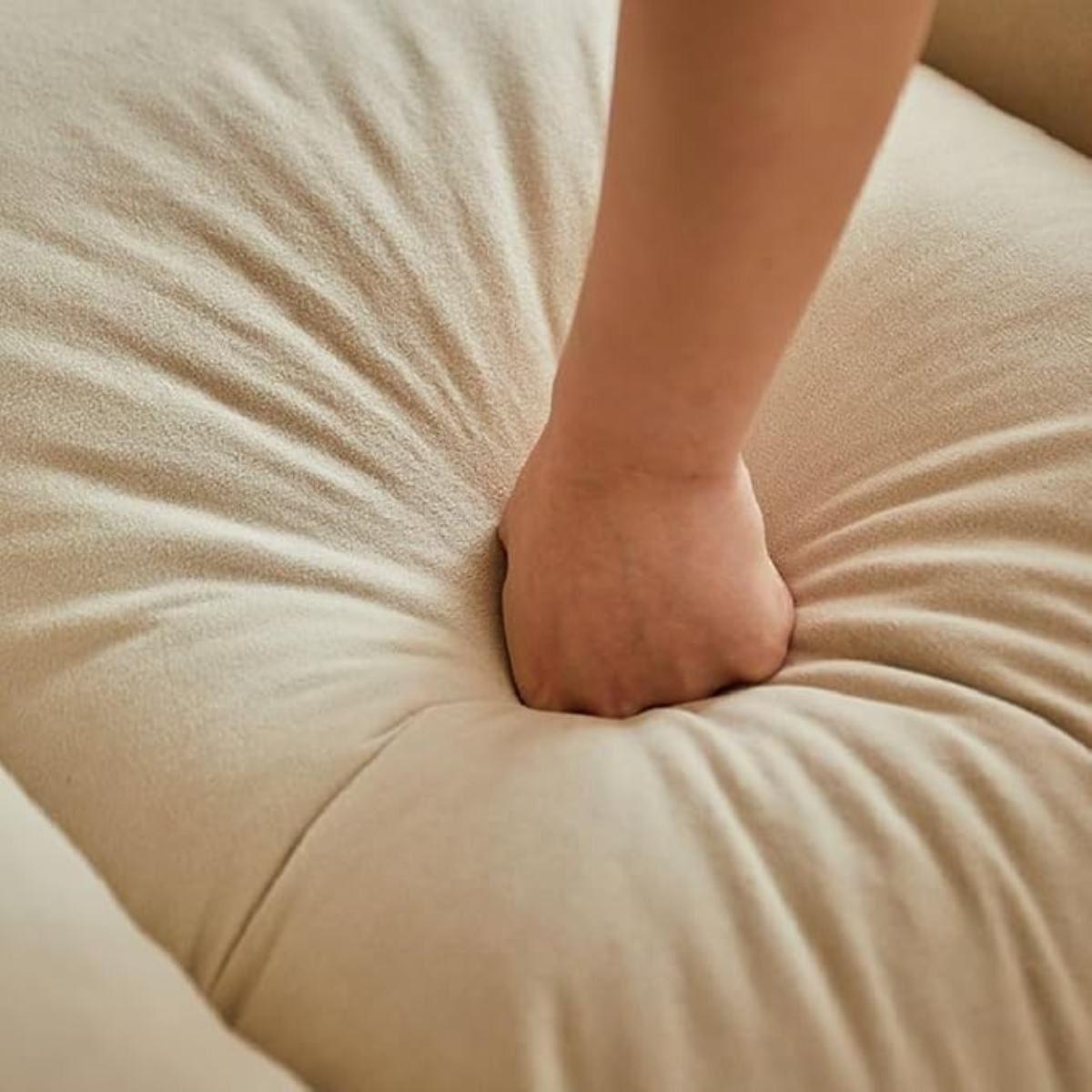 A close-up of a person's hand pressing down into the soft, textured beige fabric of a cushion or sofa.