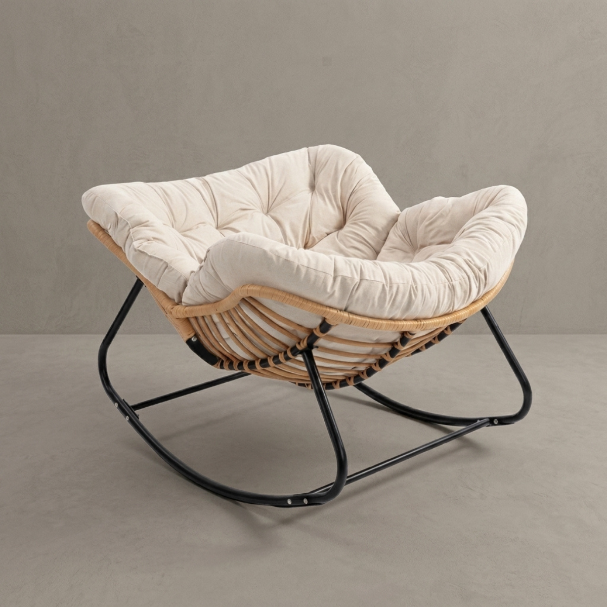 A modern wicker rocking chair with a tufted cream cushion and a black metal rocking base, set against a neutral gray textured wall and floor.