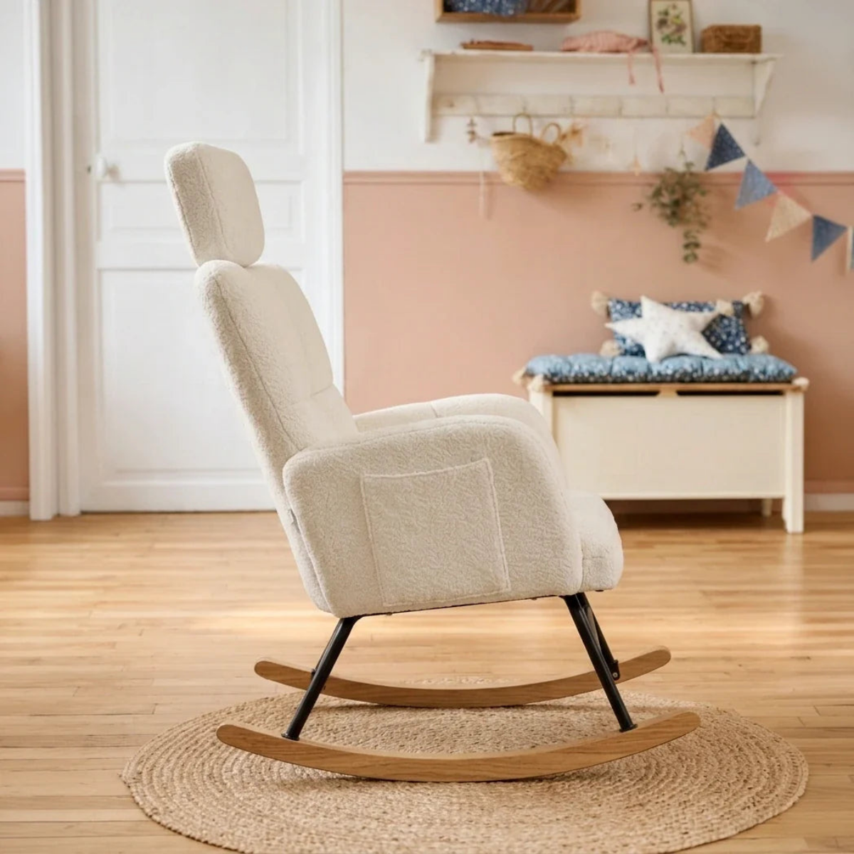 A cream bouclé rocking chair with a headrest and wooden rockers, shown in a styled nursery room setting on a woven rug.